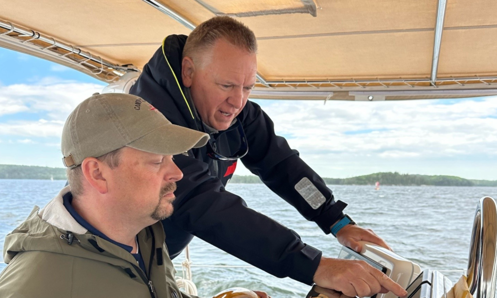 Two members of the ProInfoNet team, Jim Rogers and Jason Gay, navigating a boat during a team sailing retreat.